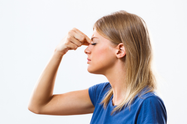 Mulher tocando a testa com expressão de dor, representando sintomas de sinusite.