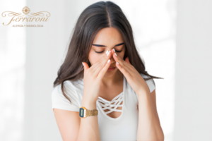 Mulher sentada tocando a região do nariz e dos olhos, aparentando desconforto respiratório.