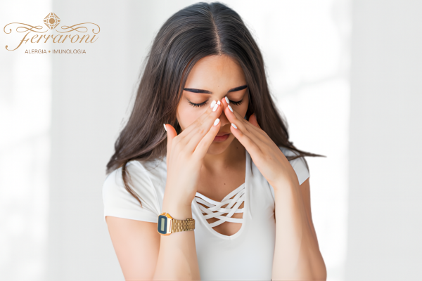 Mulher sentada tocando a região do nariz e dos olhos, aparentando desconforto respiratório.
