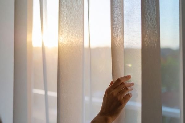 Janela aberta com entrada de luz solar e ventilação em quarto residencial.
