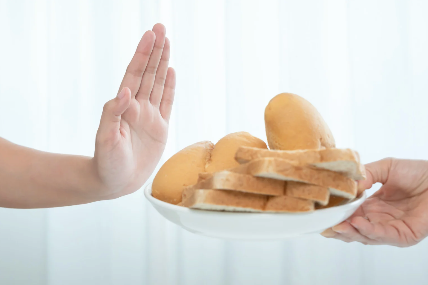 Pessoa recusando prato com pães, representando alergia alimentar ou intolerância ao trigo ou glúten.
