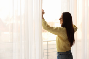 Mulher abrindo a janela do quarto para arejar o ambiente e evitar crises alérgicas