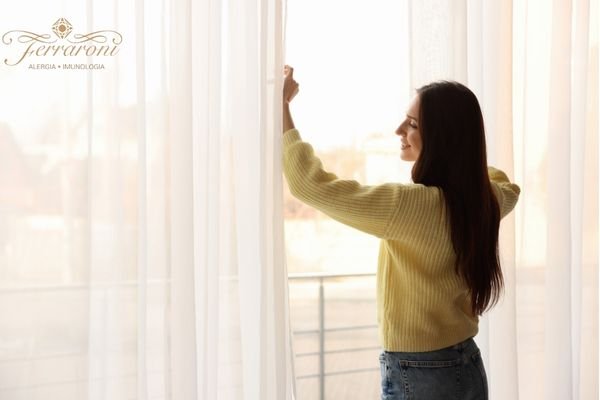 Mulher abrindo a janela do quarto para arejar o ambiente e evitar crises alérgicas
